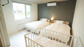 A bedroom with two beds, a window, a radiator, and a white crib. - Private Villa Yuki no oto (Furano-shi)