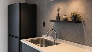 A modern kitchen with a black refrigerator, a double sink, and a countertop with a built-in oven. - Private Villa Yuki no oto (Furano-shi)