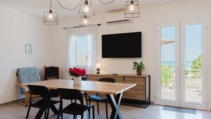Een moderne eethoek met een houten tafel, zwarte stoelen, een potplant en een aan de muur bevestigde televisie.