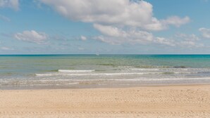 Een strand met een zandstrand, een rustige zee en een zeilboot in de verte.