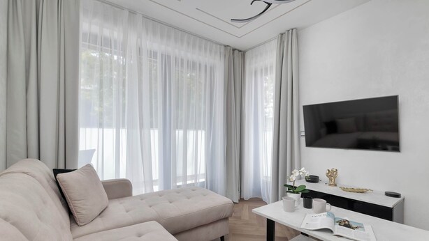 Un saló modern amb un sofà, una televisió de pantalla plana, una taula de centre i cortines de tela fina.
