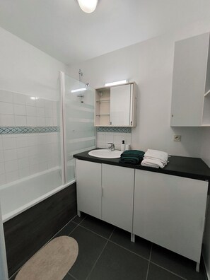 Une salle de bain avec une douche à parois de verre, un lavabo avec un miroir au-dessus et un porte-serviettes avec des serviettes pliées.
