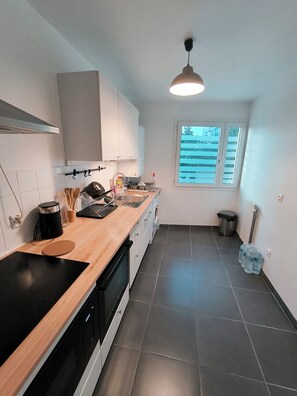 Une cuisine moderne avec un plan de travail noir, des armoires blanches, une fenêtre avec des stores et un luminaire suspendu.