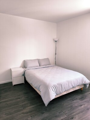 Une chambre à coucher au style minimaliste, avec un lit, une table de chevet et une lampe sur pied.