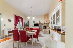 A dining area with a table set for four, red chairs, a white cabinet with glass doors, and a television in the background. - Villa Armonia Cordis (Sava)