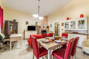 Un comedor con una mesa dispuesta para cuatro, sillas rojas, un televisor y una zona de cocina con armarios y un reloj.