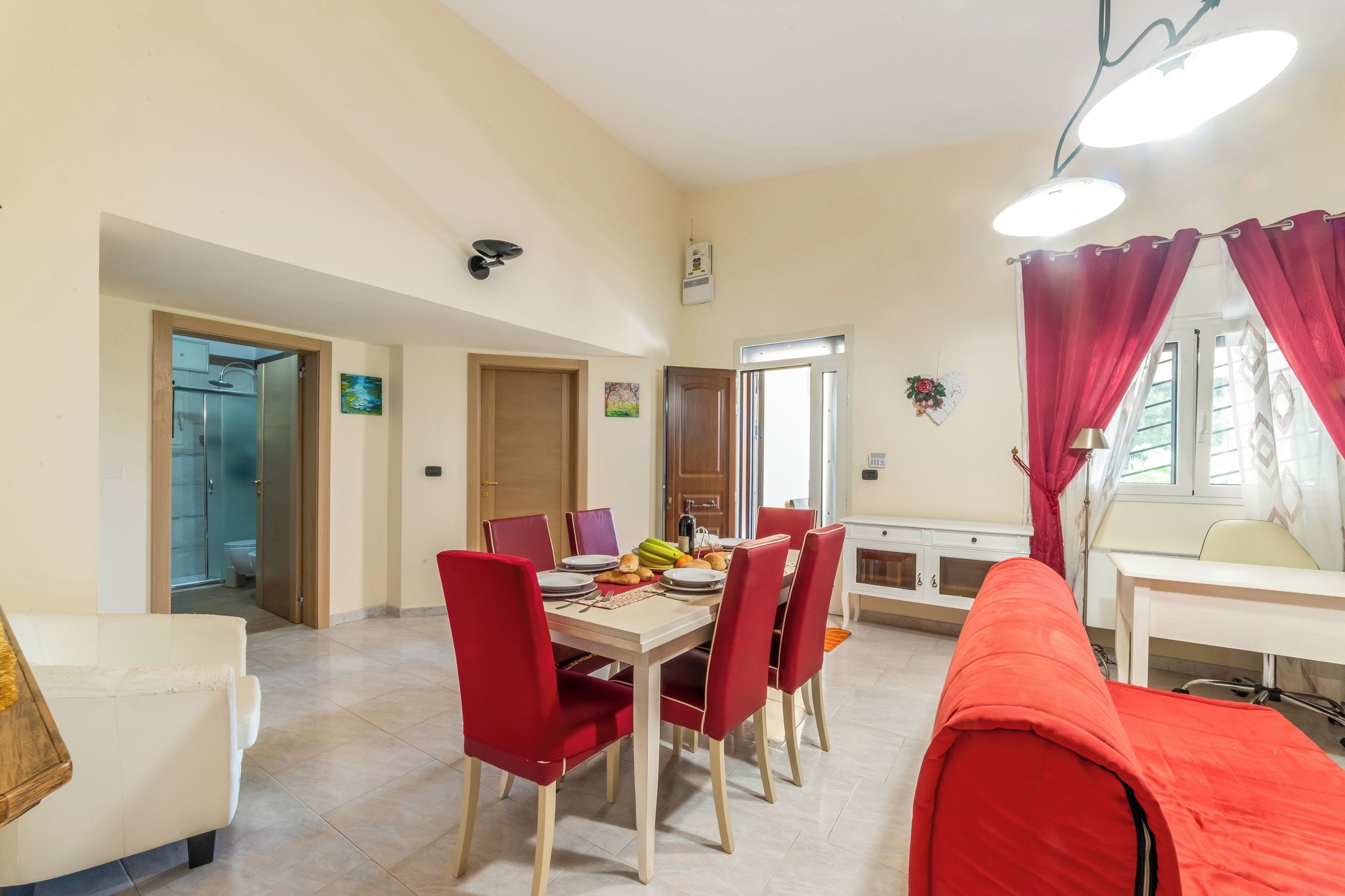 A dining area with a table set for four, red chairs, a white sofa, and a red couch.