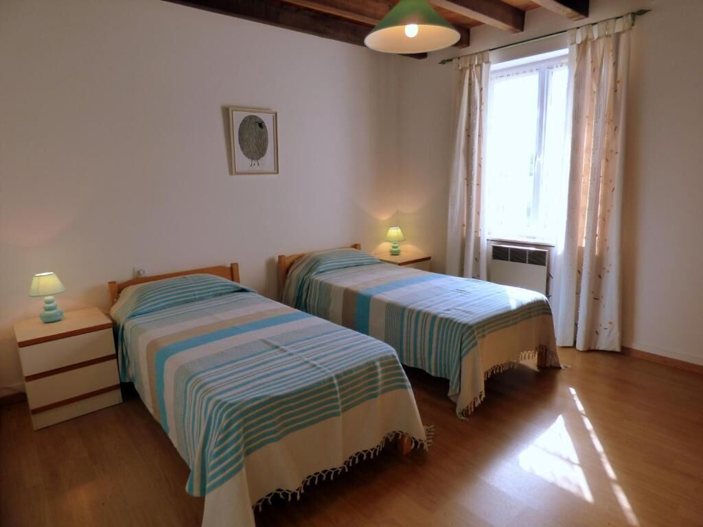 A room with two beds, a nightstand with a lamp, a framed picture on the wall, and a window with curtains.