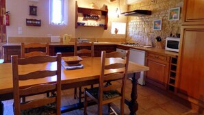 Una mesa de comedor de madera con sillas, una cocina con paredes de piedra, armarios de madera y un microondas.