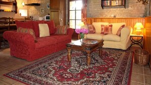 Una sala de estar acogedora con un sofá rojo, un sofá color crema, una mesa de centro de madera y una alfombra estampada.