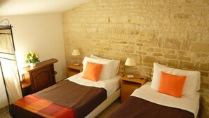 Habitación con dos camas, cada una con manta y almohadas, una mesita de noche de madera, una lámpara y una pequeña mesa con una planta.