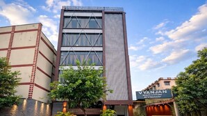 Un edificio de varios pisos con un diseño arquitectónico moderno, que presenta una entrada destacada con un cartel para un restaurante llamado 'Vyanjan'.