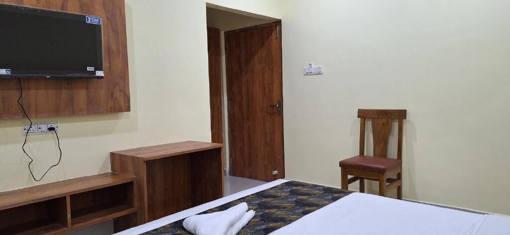 A bedroom with a bed, a wooden chair, a TV mounted on the wall, and a door.