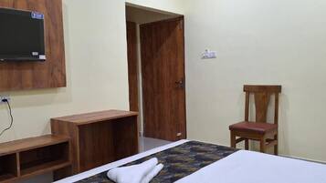 A bedroom with a bed, a wooden chair, a TV mounted on the wall, and a door.