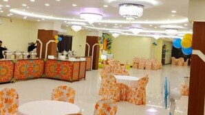 Un amplio salón con mesas y sillas redondas, una zona de recepción con mostrador y un techo decorativo.