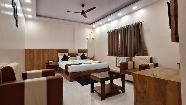 Habitación de hotel con cama, dos sofás, una mesa de centro, televisor y ventilador de techo.