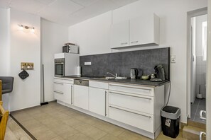 A modern kitchen with white cabinetry, a grey backsplash, and a built-in microwave.