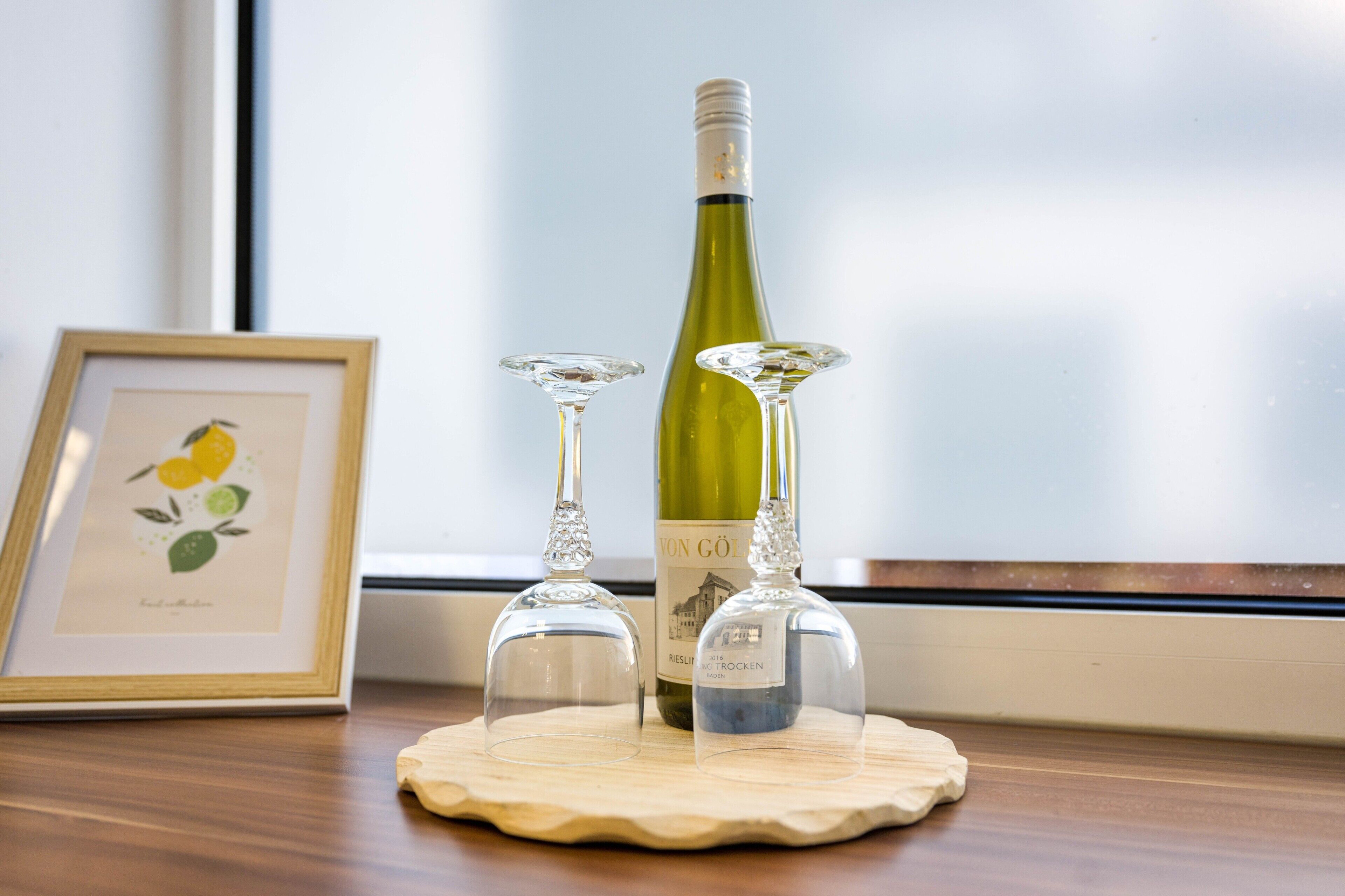 A wine bottle and two wine glasses on a wooden coaster.