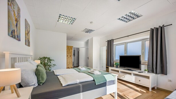A modern hotel room with a large bed, a TV, a desk, and a window with curtains.