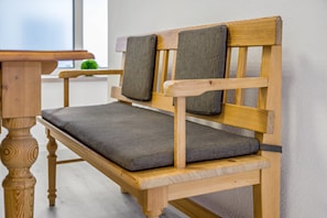 A wooden bench with a cushioned seat and backrest, positioned against a wall.
