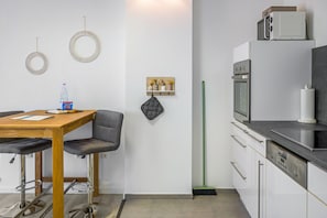 Una cocina moderna con una mesa de madera, taburetes de bar, una escoba y un microondas.