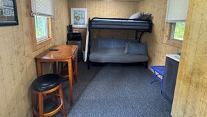 Une petite pièce comprenant un lit superposé, une petite table avec une chaise, un bureau et un cadre photo accroché au mur.