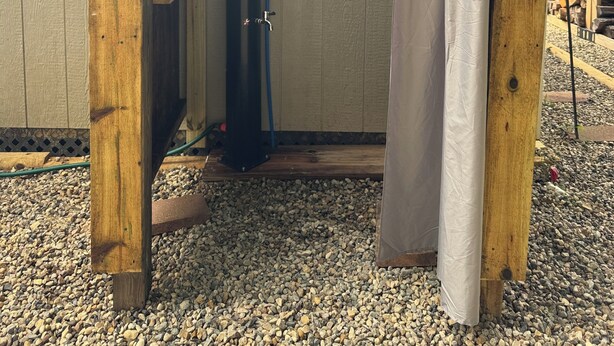 Une structure de pergola en bois comprenant un espace douche, une fenêtre et un sol en gravier.