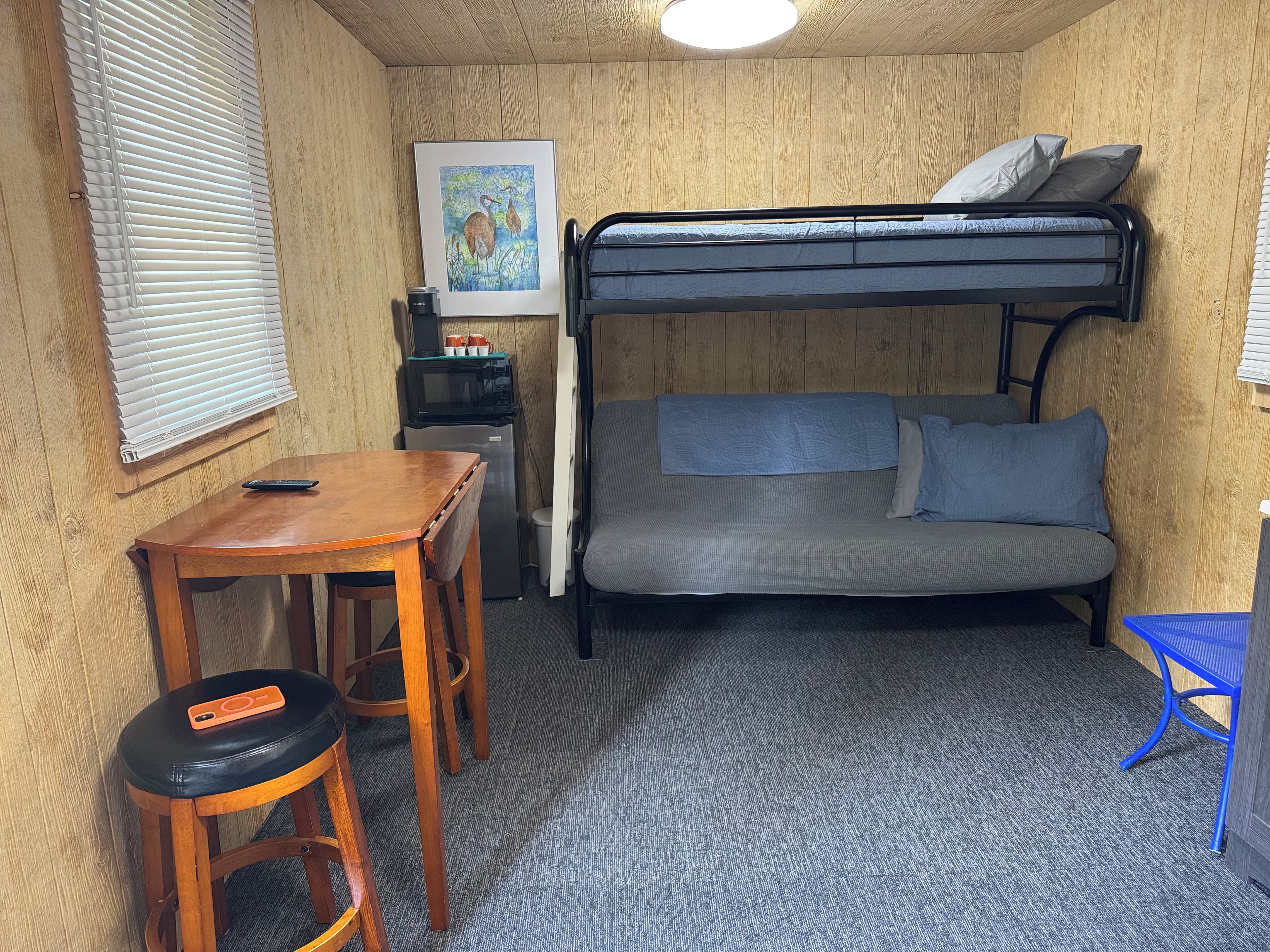 A compact room with a bunk bed, a small table with a chair, a microwave, and a refrigerator.