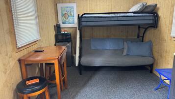 A compact room with a bunk bed, a small table with a chair, a microwave, and a refrigerator.
