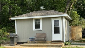 Une petite maison de plain-pied avec un porche à l’avant, un barbecue et une chaise.