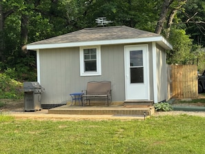 A small, single-story house with a porch, a grill, and a chair. - Top O’ The World Tiny Cabin, Cozy 1-Room cabin on a lake in Grass Lake, MI (Grass Lake)