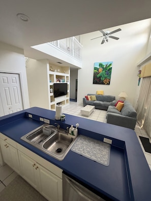 Eine moderne Küche mit blauer Arbeitsplatte, einer integrierten Spüle und einem Essbereich mit grauem Sofa und einem Bild an der Wand.