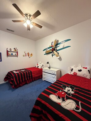 Ein Schlafzimmer mit zwei Betten, einem Deckenventilator, einer Kommode und einem Wandsticker eines Flugzeugs.