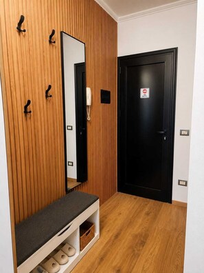 A hallway with a wooden wall, a bench with shoe storage, a mirror, and a black door with a 'No Entry' sign. - Modern Central Tirana Apartment with Free Parking & Fast WiFi (Tiranë)