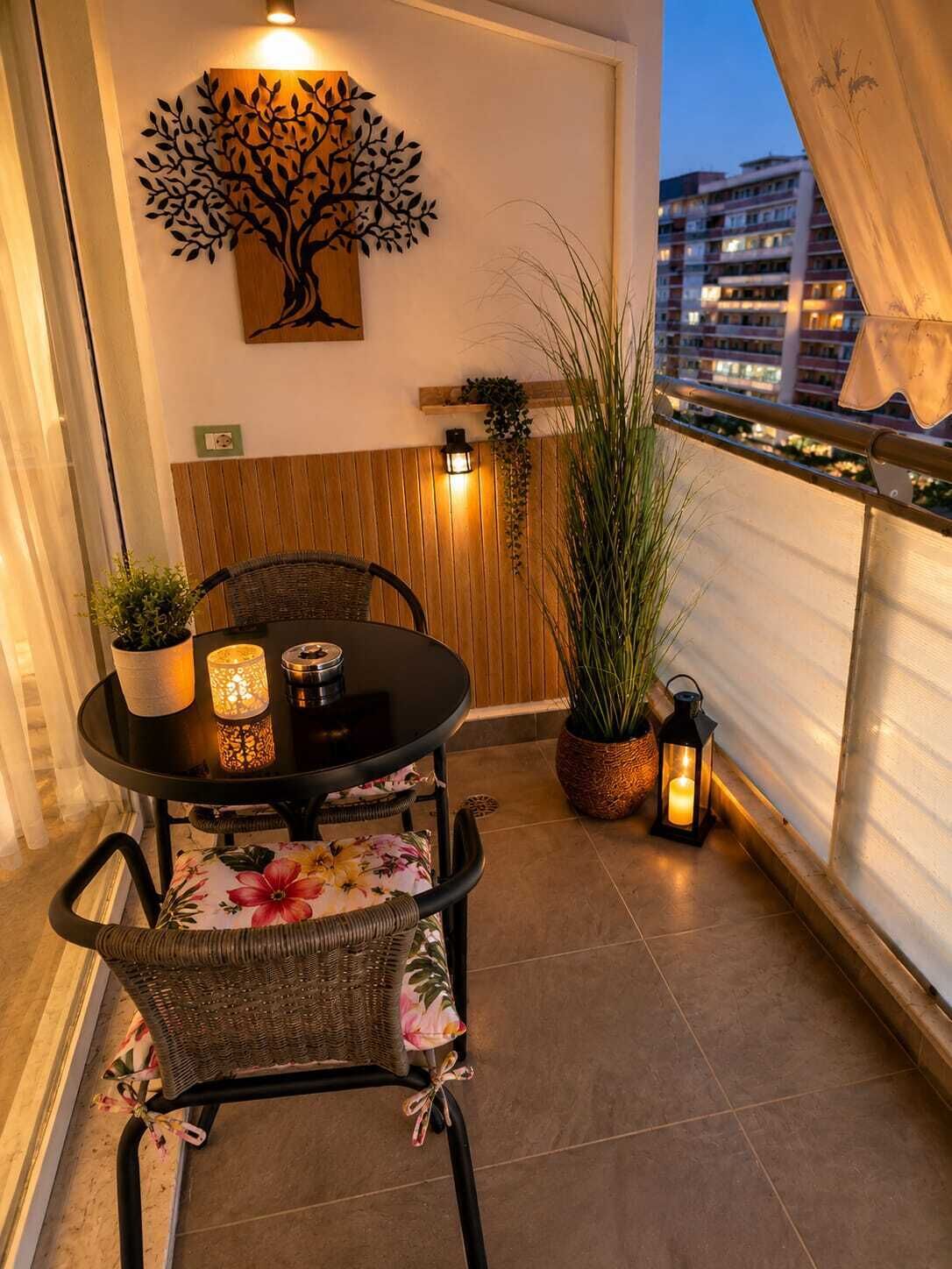 A balcony with a table and chairs, a decorative tree wall art, a potted plant, and a railing.