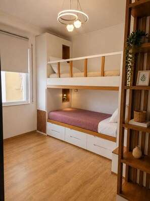 A bunk bed room with a wooden floor, a window, and a shelf with decorative items. - Modern Central Tirana Apartment with Free Parking & Fast WiFi (Tiranë)