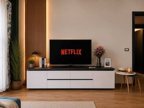 Un salon moderne avec un téléviseur à écran plat affichant le logo « NETFLIX », un meuble de rangement blanc, une petite table avec un vase et une plante en pot.