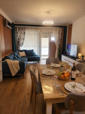 A modern living room with a sofa, dining table set for two, and a television. - Modern Central Tirana Apartment with Free Parking & Fast WiFi (Tiranë)