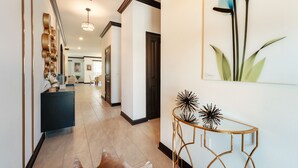 A hallway with a dark blue console, a glass table with a gold frame, and a large floral painting on the wall. - 4359-Rhyme (Kissimmee)