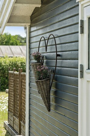 Ein Haus mit grauer Außenwand, einem Holzzaun und einem herzförmigen Metallpflanzgefäß mit Blumen.