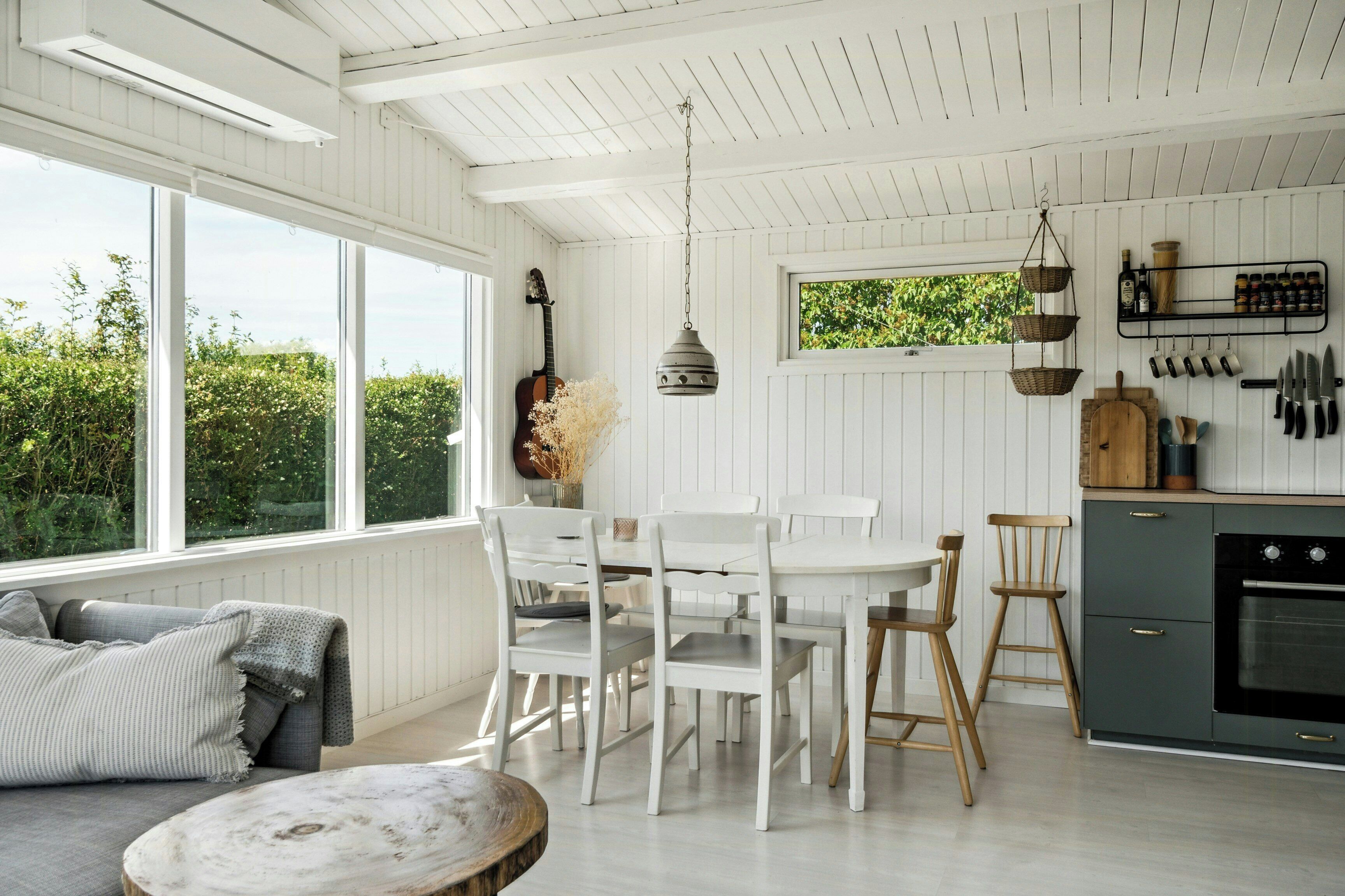 A kitchen with white cabinetry, a dining table with chairs, a hanging light fixture, and a window with a view of greenery.