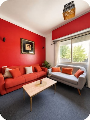 Ein Wohnzimmer mit einem roten Sofa, einem grauen Sofa, einem Holztisch und einem Bild an der Wand.