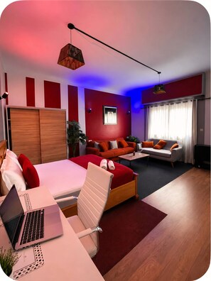 Ein modernes Schlafzimmer mit einem Bett, einem Schreibtisch mit Laptop, einer Couch und einem Couchtisch.