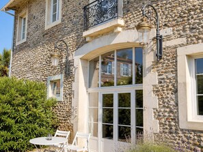 A stone building with a balcony, a large window, and a table with chairs outside. - A place to recharge your batteries at the foot of the Pyrenees (Meillon)