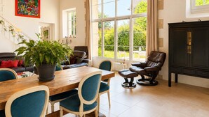 Amplia habitación con una mesa de comedor de madera, sillas tapizadas en azul, un sofá de cuero y un amplio ventanal con vistas a la vegetación.