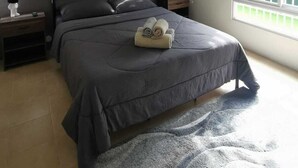 Een slaapkamer met een bed, een plafondventilator, een airconditioner, een raam met jaloezieën en een aan de muur bevestigd kunstwerk.