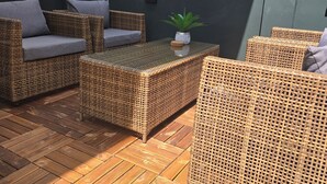 Een terras met rieten meubels, een kleine tafel en een potplant.