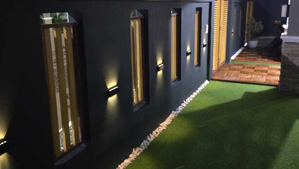 Een modern gebouw met een donkere gevel, verlichte ramen en een klein buitengebied met kunstgras en een stenen rand.