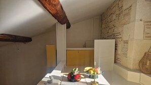 A kitchen with a wooden ceiling beam, a stone wall, and a small table with fruits and a vase. - Dupleix and an open-air terrace (Saint-Gilles)