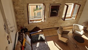 A room with a stone wall, a window with a view, a sofa, a chair, and a small table. - Dupleix and an open-air terrace (Saint-Gilles)